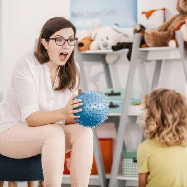 A sensory game with a blue ball played by a professional child therapist with a kid in a family support center.