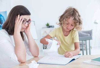 Stressed psychotherapist having a headache during a meeting with a rebellious child with behavioral disorders. The kid is tearing sheets of paper from the notebook.