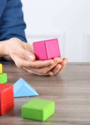 ABA therapist with colorful building blocks at wooden table, closeup