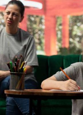 During a therapy session, an adolescent girl practices drawing to help with behavioral therapy and emotional regulation. The therapist and mother provide support for her mental wellbeing.