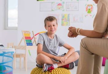 Child psychologist concept, happy little boy smiling sitting on pouf in child mental health centre