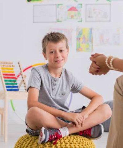 Child psychologist concept, happy little boy smiling sitting on pouf in child mental health centre